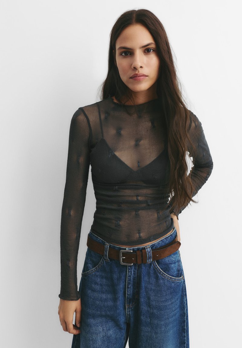 Genomskinlig svart långärmad topp med en figurnära bodice och mönstrad textur, ihopparad med högmidjade blå denimjeans och ett brunt skärp.