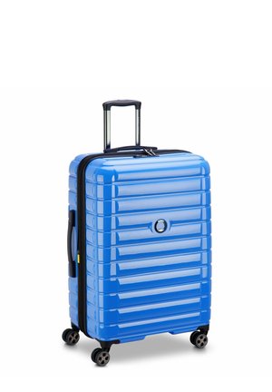 Valigia rigida blu con texture rigata, cerniera nera e maniglia estraibile. Presenta quattro ruote per la mobilità e un accento con logo circolare.