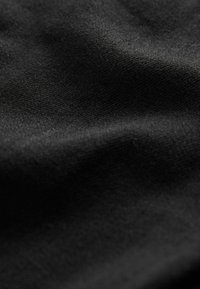Tela negra con una superficie lisa y ligeramente texturada, que muestra suaves pliegues y variaciones en la luz, típicas de los materiales tejidos.
