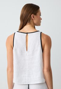 Top sans manches en lin blanc avec une bordure noire et un détail en trou de serrure au dos. Texture douce et coupe décontractée, idéale pour les superpositions ou un style décontracté.