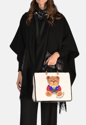 Donna in abbigliamento nero che tiene in mano una borsa bianca con un design di un orsetto colorato e il testo "Rue Madam Paris" sul davanti.