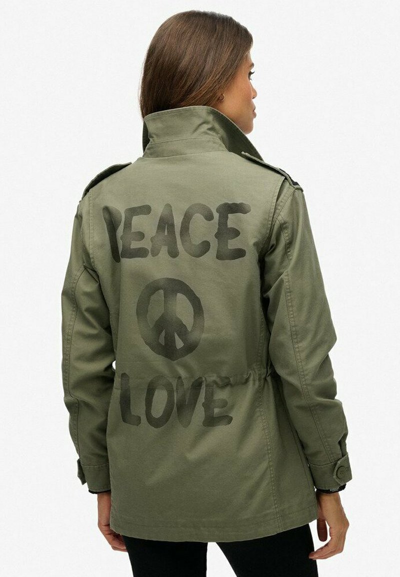 Chaqueta verde olivo con un cuello alto, que presenta "PAZ", un símbolo de paz y "AMOR" impresos en gran tamaño en la parte posterior en fuente negra.