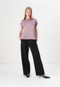 Lavender short-sleeve top with rolled cuffs paired with black wide-leg trousers and pointy black heels, set against a white background.