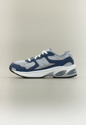 Chaussure de course grise et bleu marine avec panneaux en mesh et en suède, lacets blancs, semelle amortie et logo sur le côté.