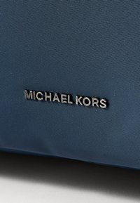 Tumši zila neilona somiņa ar teksturētu virsmu un sudraba metāla "MICHAEL KORS" logo priekšpusē.