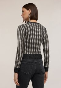 Gestreifter Pullover in Schwarz und Weiß mit geripptem Saum und Bündchen, der ein strukturiertes Strickdesign aufweist. Das Model trägt dunkle Jeans.