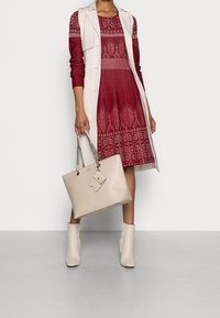 Röd stickad klänning med geometriska mönster, krämfärgad trenchcoat, beige handväska med kedjehandtag och ljusbeige ankelskots.
