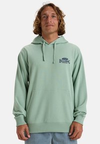Sudadera de color verde claro con un bolsillo frontal, capucha ajustable con cordones y logo de Billabong en el pecho. Diseño de tela suave y ajuste relajado.