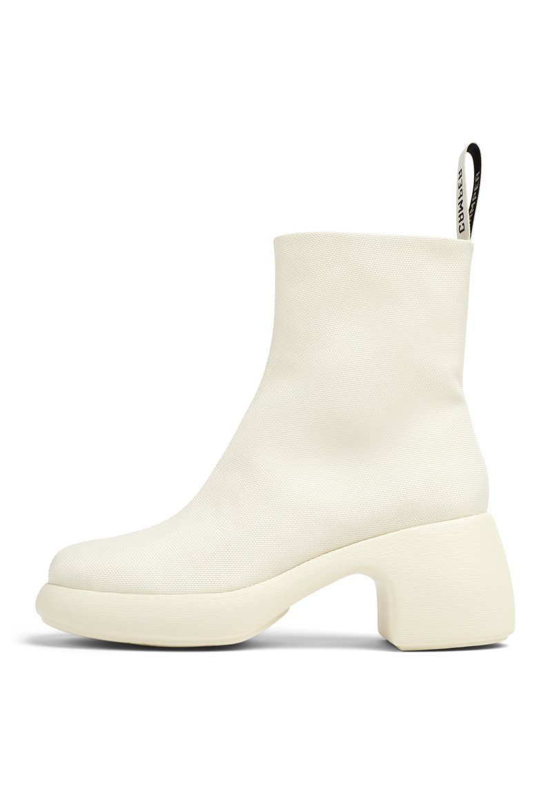 Valkoinen nilkkaboots, joka on valmistettu teksturoidusta materiaalista ja jossa on paksu, kaareva korko. Varustettu vetoketjulla takana ja sileällä, pyöreällä kärjellä.