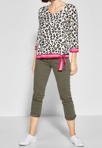 Vit leopardsmönstrad topp med rosa detaljer och sidoknytning, kombinerad med olivgröna croppade byxor och vita sneakers.