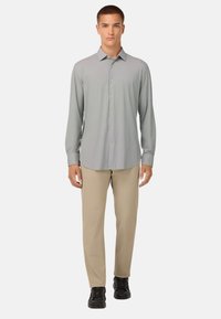 Camicia grigia a maniche lunghe con bottoni, caratterizzata da un sottile motivo a scacchi, abbinata a pantaloni beige e sneakers nere. Colletto strutturato e vestibilità rilassata.