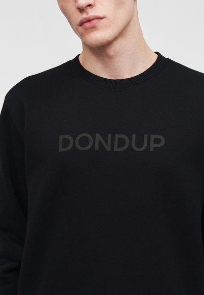 Jeune homme portant un sweat-shirt noir à col rond avec le nom de la marque DONDUP embossé sur la poitrine.