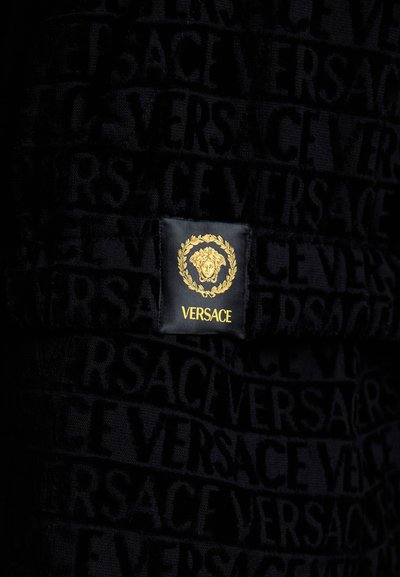 Asciugamano nero con tessuto testurizzato e motivo a logo "VERSACE" ripetuto. Include un'etichetta in oro con il logo Medusa e una corona di alloro.