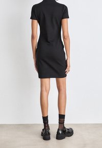 Czarna sukienka krótko rękawowa z wysokim kołnierzem, dopasowana sylwetka, gładka tekstura. W zestawie z czarnymi masywnymi butami i przezroczystymi czarnymi skarpetkami.