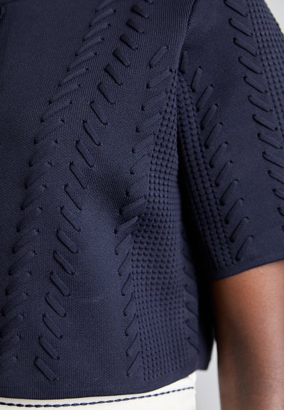 Top a maglia blu navy con strisce texture, caratterizzato da una forma aderente e maniche corte, rifinito con un orlo cucito bianco.