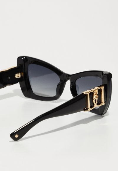 Lunettes de soleil noires en forme d'œil de chat avec des verres gris dégradés. Présentent une accent en métal doré sur le côté et une monture en plastique brillante.