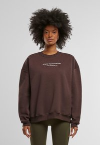 Hnědá mikina s volným střihem, žebrovanými manžetami a lemem. Na přední straně je bílý text "Aim'n Sportswear". Hladká textilie.