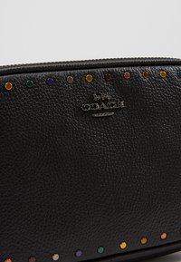 Portafoglio in pelle nera con finitura testurizzata, dettagli con borchie dorate e multicolore lungo la parte superiore, e targhetta con logo argentata.