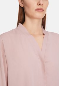 Helle rosa Bluse mit Stehkragen, aus einem glatten Material, mit subtilen Nähten und einem lockeren Schnitt.