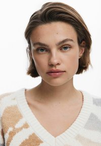 Pulover tricotat cu decolteu în V, având un model abstract în nuanțe de crem, bej și gri. Textură moale și detaliu dublat cu nervuri în jurul decolteului.