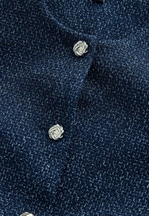 Navy textured cardigan featuring silver knotted buttons, crafted from a soft fabric with a subtle sheen and intricate knit pattern.