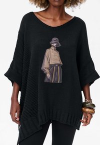 Czarny, oversize sweter dzianinowy z intensywną graficzną ilustracją postaci w pasiaku i czapce, z prążkowanymi rękawami i dolnym wykończeniem.