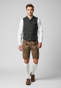 Abbigliamento tradizionale maschile caratterizzato da un gilet senza maniche scuro, pantaloni corti marroni con dettagli ricamati, calze lunghe bianche e scarpe marroni.