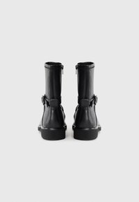 Black leather boots with a straight shaft, rear zippers, and side buckles. Thick rubber soles with slight texture and rounded edges.