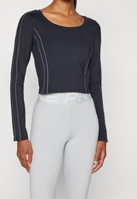 Schwarzes, langärmliges, kurzes Oberteil mit Kontrastnähten, Rundhalsausschnitt und weichem Stoff, kombiniert mit hellgrauen, enganliegenden Leggings mit Logo-Band.