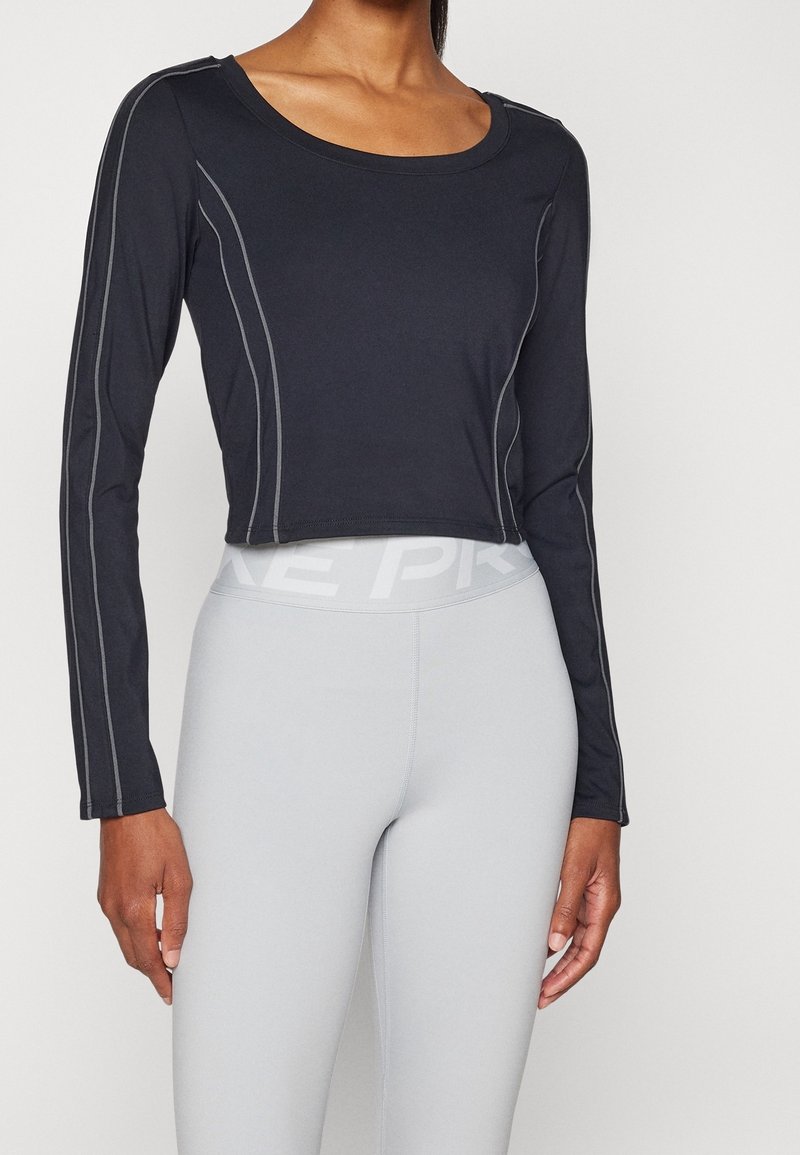 Schwarzes, langärmliges, kurzes Oberteil mit Kontrastnähten, Rundhalsausschnitt und weichem Stoff, kombiniert mit hellgrauen, enganliegenden Leggings mit Logo-Band.