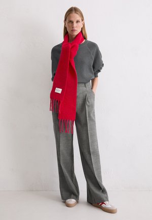 Red wool scarf with fringes, gray sweatshirt, and gray plaid trousers. Sneakers with contrasting accents complete the outfit.