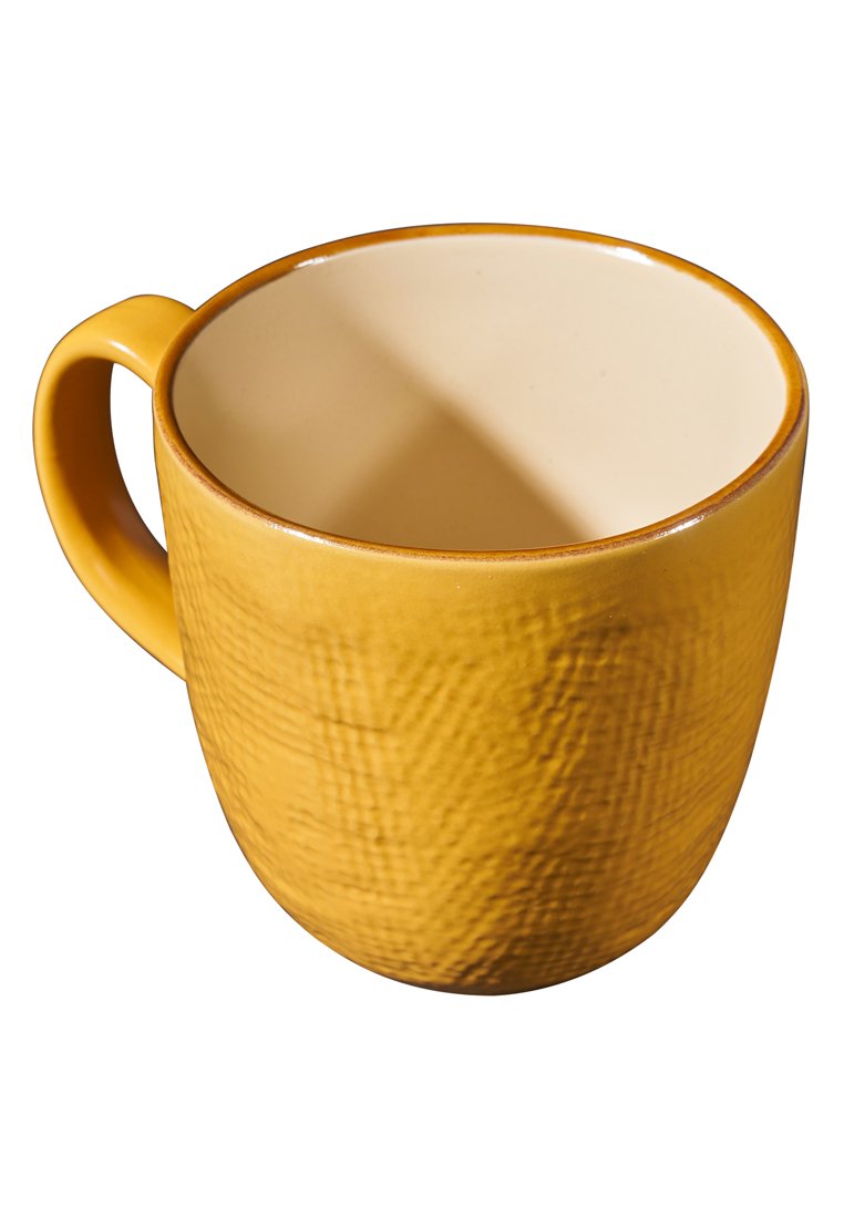 Ceramiczny kubek o chropowatej, matowej, musztardowo-żółtej powierzchni z gładkim, kremowym wnętrzem. O okrągłym kształcie z ergonomicznym uchwytem.