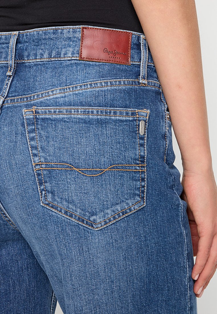 Blaue Jeans aus Denim verfügen über ein auffälliges braunes Lederpatch am Bund, sichtbare Nähte und ein rückseitiges Taschendesign mit kontrastierendem Faden.