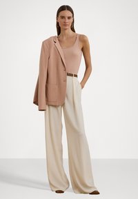 Beige ullblazer med en enda ficka hängande över armen. Ljusrosa linne kombinerat med krämfärgade vida byxor och ett brunt bälte.