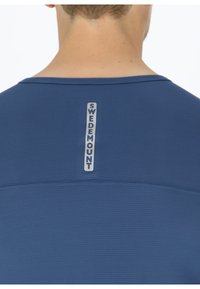 Camicia strutturata blu navy con scollo rotondo. Presenta un'etichetta verticale argentata con la scritta "SWEDEMOUNT" nella parte alta posteriore.