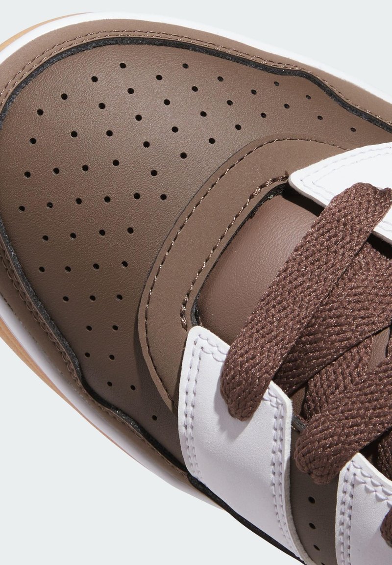 Brown sneaker with perforated leather upper, contrasting white accents, and textured brown laces. Features a gum rubber sole.