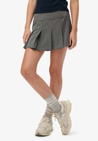 Grijze krijtstreeppantalon met geplooid ontwerp, gecombineerd met lichtgrijze gestreepte sokken en beige sportschoenen. Eenvoudige, functionele styling.