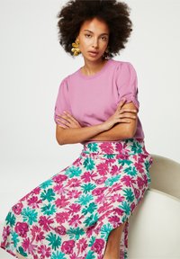 Hellblaues T-Shirt mit kurzen Puffärmeln, kombiniert mit einem knielangen, blumengemusterten Rock, der rosa und türkisfarbene Blumen auf einem cremigen Hintergrund zeigt.