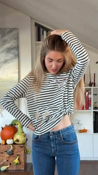 White and black striped long-sleeve shirt with small embroidered details. Worn with high-waisted blue jeans featuring decorative stitching.