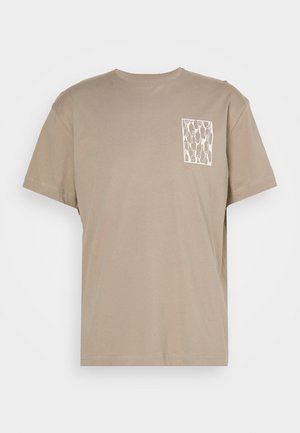 Camiseta de algodón beige con cuello redondo y mangas cortas. Presenta un estampado geométrico blanco en un bolsillo cuadrado en el pecho izquierdo.