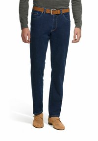 Jeans en denim bleu foncé avec des poches avant, une ceinture en cuir marron avec une boucle en argent, et des détails de couture clairs ; accompagnés de chaussures marron.