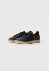 Sorte sneakers med en struktureret overdel, tre sorte striber og et guldlogo. Med en sål af gummirubber og et lavprofildesign.
