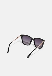 Occhiali da sole in plastica nera con lenti grigie sfumate, montatura quadrata ampia e sottili bracci metallici color rosa oro con dettagli decorativi.