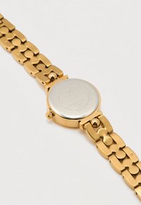 Gouden roestvrijstalen horloge met een ronde kast, schakelarmbandontwerp en een gladde, reflecterende achterkant met gegraveerde merknaam.
