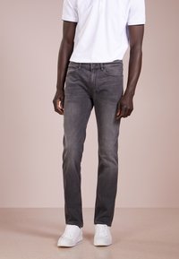 Gray denim jeans with a straight-leg fit, slight fade, and front pockets, paired with white sneakers and a white polo shirt.