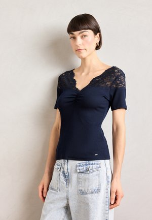 Marineblauw t-shirt met korte mouwen en kanten accenten op de schouders en een geplooide v-hals. Geribbelde textuur, gecombineerd met lichtblauwe, hoogwaardig broek.