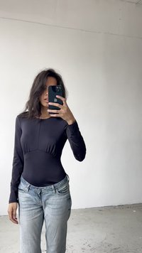 Black long-sleeve bodysuit with a fitted design and a seam at the bust, paired with light blue denim jeans. Smooth texture, minimal hardware.