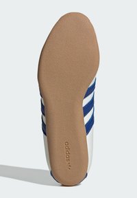 Adidas-skon soles med en slät brun gummikonstruktion, med blå och vita ränder och Adidas-logotypen präglad på sidan.