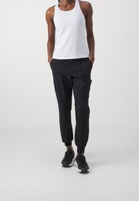 Vit tanktopp, svarta joggers med elastisk midja och sidofickor, samt svarta sneakers. Materialet verkar lätt och slätt.