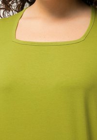 Top verde a maniche corte con ampia scollatura quadrata. Tessuto morbido e testurizzato con cuciture lisce. Il colore è una tonalità vibrante e uniforme.